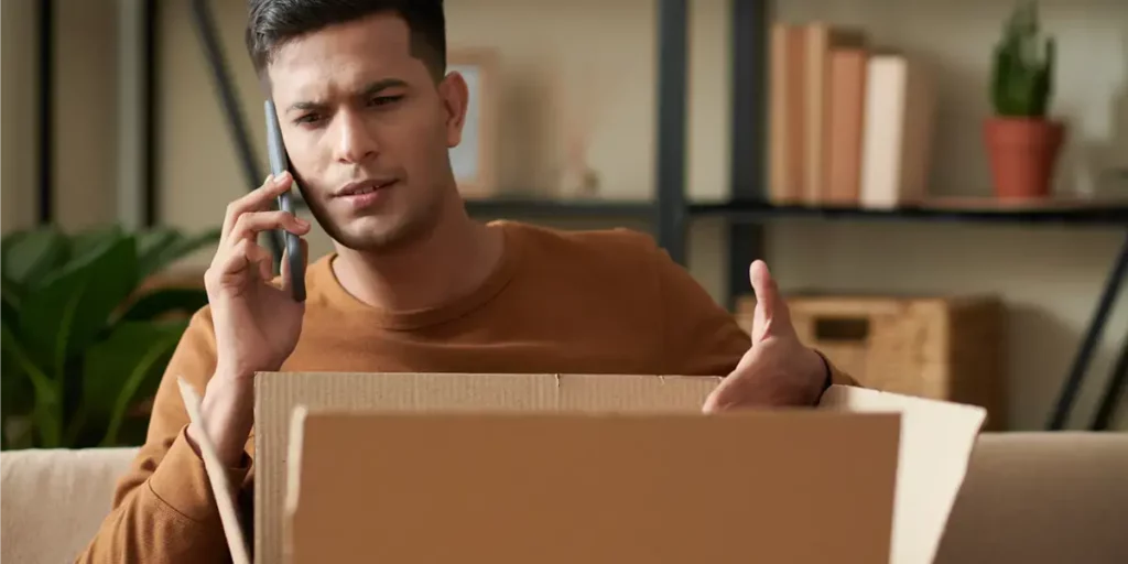 Man on the phone, opening a box unsatisfied.
