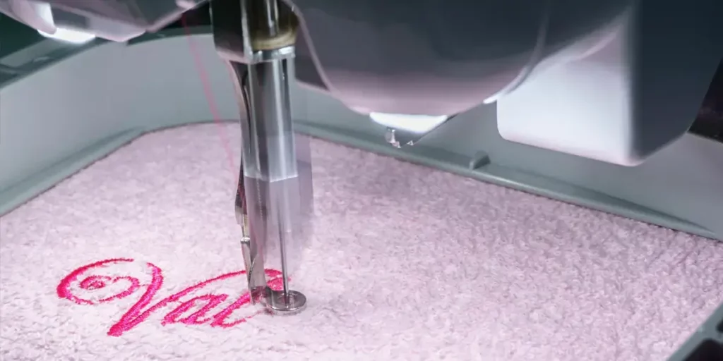 Close-up of a machine embroidering on a pink towel