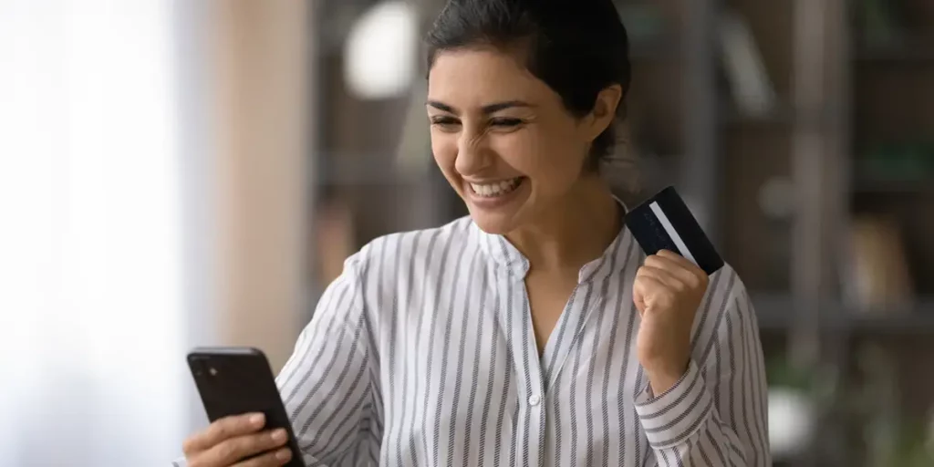 Woman holding a phone and credit card with a happy expression
