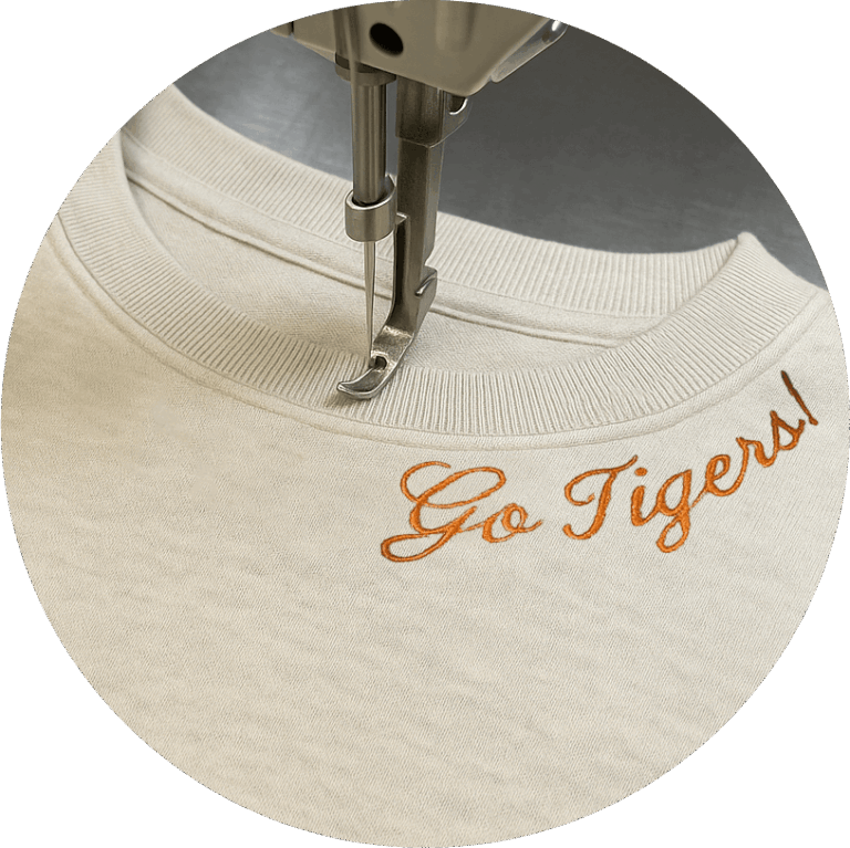 Closeup Image of a tan sweatshirt with the phrase "Go Tigers!" Embroidered around the neckline.