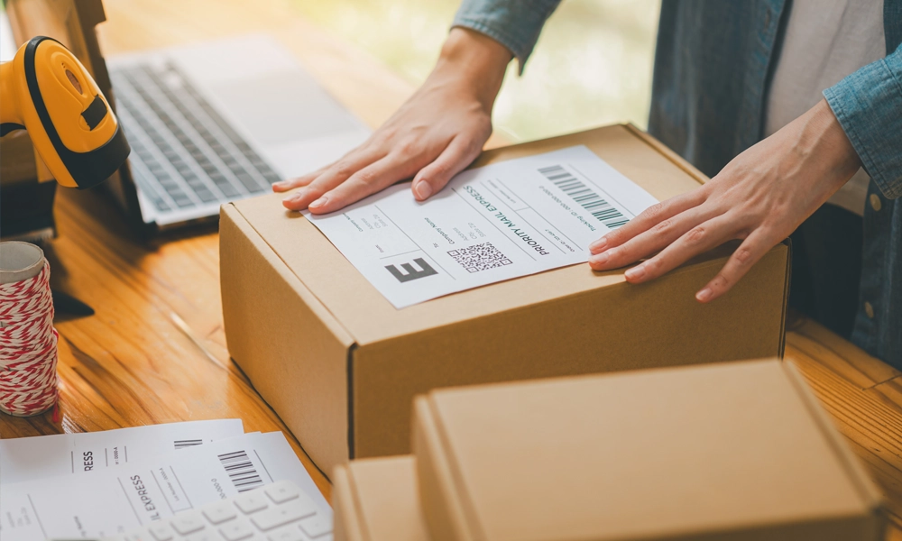 Male entrepreneur placing a shipping label on a brown shipping box.